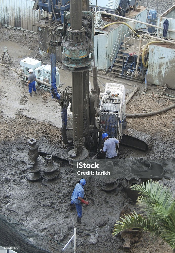 Construction site: maintaining a hole drilling machine Men at work at construction site, removing mud from machine Drill Stock Photo