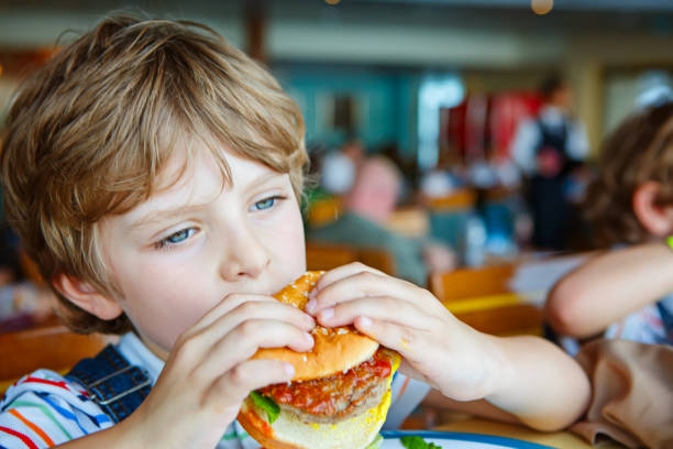 istock Cute healthy preschool boy eats hamburger sitting in school canteen 1056851582