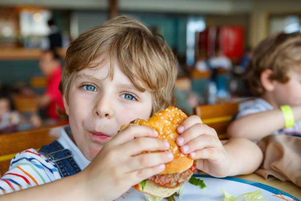 istock Cute healthy preschool boy eats hamburger sitting in school canteen 1056851588
