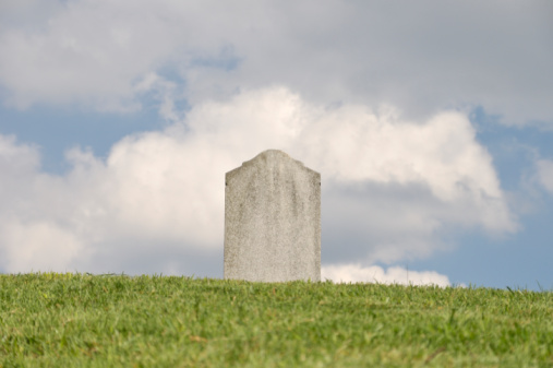 A blank tombstone against a sky with fluffy clouds..