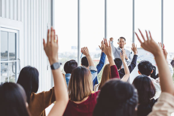 gruppo di uomini d'affari alzano la mano per concordare con il relatore nel seminario della sala riunioni - cheering arms raised women university foto e immagini stock