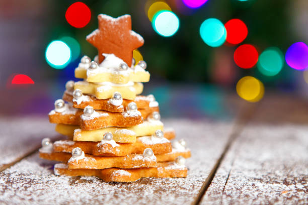 Home made baked Christmas gingerbread tree as a gift for family and friends on wooden background. With colorful lights from Christmas tree on background. With icing sugar gift for xmas.