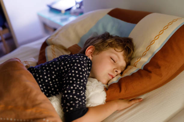 piccolo bambino in età prescolare che dorme a letto con una lampada colorata. - baby sleeping bedding teddy bear foto e immagini stock