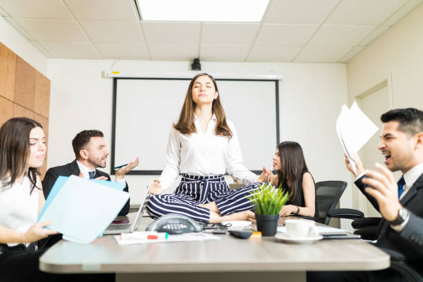 Easygoing Businesswoman Keeping Calm In Stressing Situation Young businesswoman meditating in lotus position while colleagues yelling during negotiation in office cross legged photos stock pictures, royalty-free photos & images