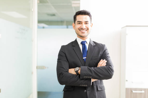 Handsome Businessman In Suit Smiling At Workplace Young and powerful Hispanic lawyer standing arms crossed in office salesman photos stock pictures, royalty-free photos & images