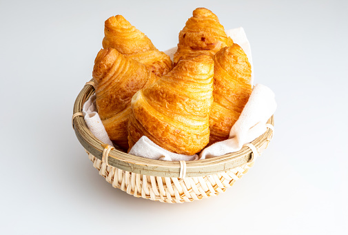 Butter croissants in small wicker basket. On white background.
