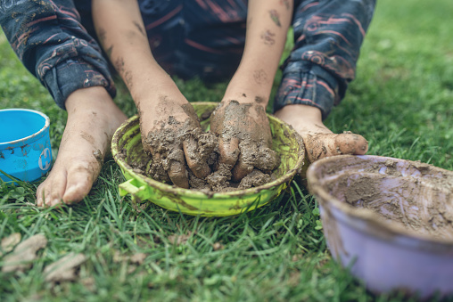 Retro image of toddler child sitting in grass playing with mud having his hands and feet all dirty.