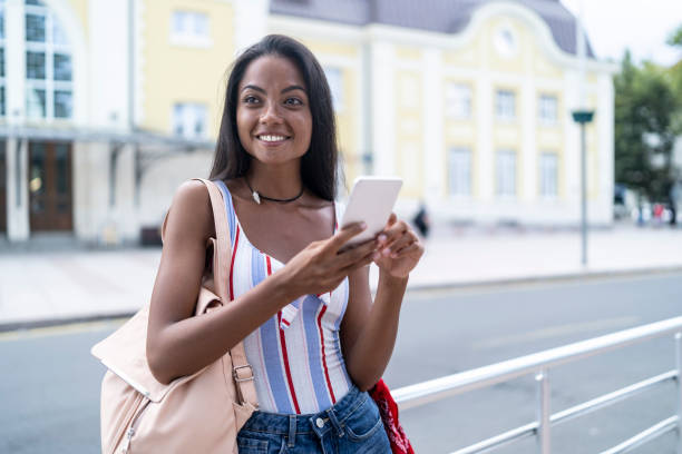 istock Smiling woman using smart phone on street 1056884608