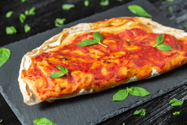 istock Closed calzone pizza with dry-cured ham, mozzarella cheese, Basil and tomatoes 1056897556