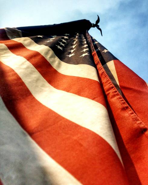 American flag flying on wooden pole on patio of cabin at nature park outside of Houston, Texas, America. Lookup view of waving flag of USA with rustic outdoor wall lamp in natural setting