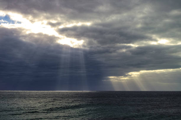 istock Dramatic dark seascape, sun's rays pass through the clouds at sunset and make spot of light on ocean water 1056906450