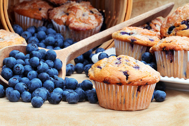 Blueberry Muffins Delicious homemade blueberry muffins with fresh blueberries spilling from a wooden spoon and wicker basket. Blueberry Muffin stock pictures, royalty-free photos & images