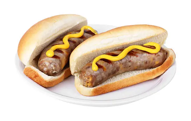 Two grilled bratwursts on buns with mustard on a plate isolated on white