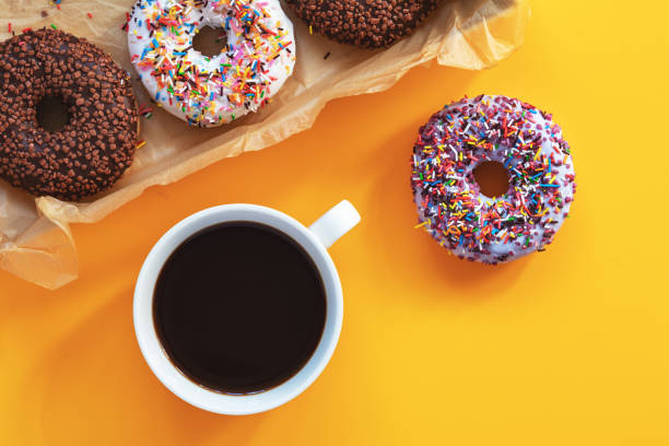 Delicious glazed donuts and cup of coffee on yellow surface