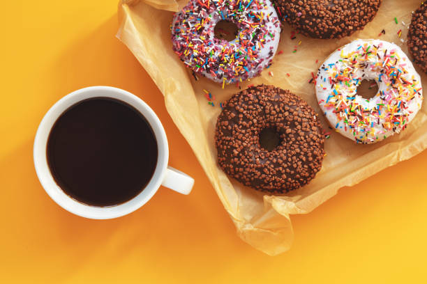 istock Delicious glazed donuts and cup of coffee on yellow surface 1056919562