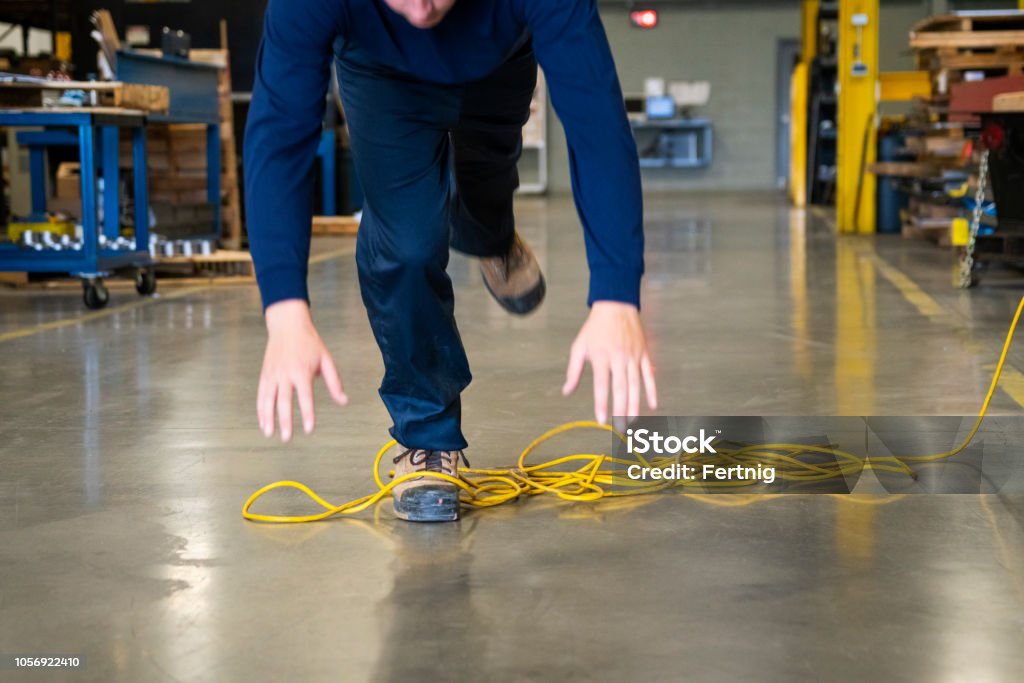 A worker tripping over an electrical cord in an industrial environment An industrial safety topic.  A worker tripping over an electrical extension cord in an industrial environment. Working Stock Photo