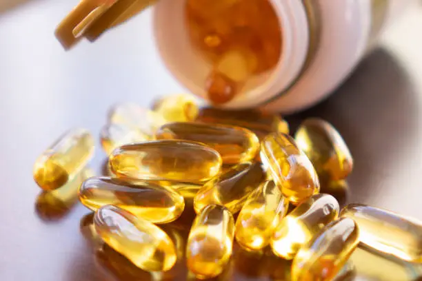 Photo of Fish oil capsules with omega 3 and vitamin D in a glass bottle on wooden texture, healthy diet concept, close up shot.