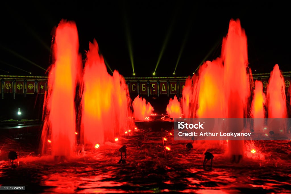 Red Fountains and Light Projections on the Victory Museum MOSCOW, RUSSIA - Impressive fountains on Square of Victors spotted with red lights and testing video mapping projections on the facade of the Victory Museum on Poklonnaya Hill in the background in one day before beginning fascinating Moscow International Festival “Circle of Light”. The popular festival took place in the Victory Park first time on September 21-25, 2018. Projection Mapping Stock Photo