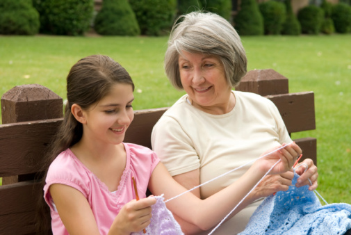 Grandmother teaching her grand daughter how to crochet on a park bench