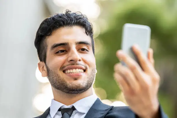 Young hispanic or middle eastern business man holding his smart phone video conferencing