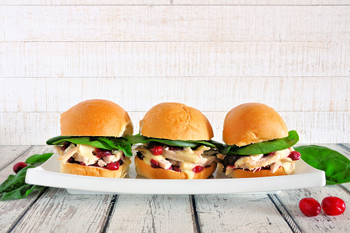 Roasted turkey sandwiches with cranberry sauce and cheese. Group on a serving plate against a white wood background.