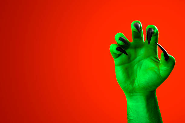 istock Halloween, nightmare creature and evil monster horror story concept with a scary zombie or demon hand with creepy long black nails isolated on orange background with a clip path cutout and copyspace 1056969924