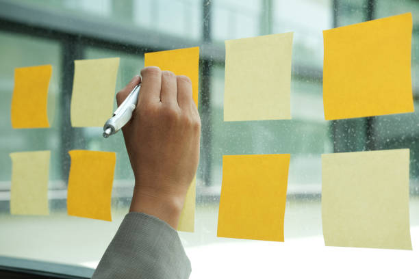 istock hand write on adhesive notes on glass wall. Sticky note paper reminder schedule for discussing creative idea & business brainstorming 1056971570