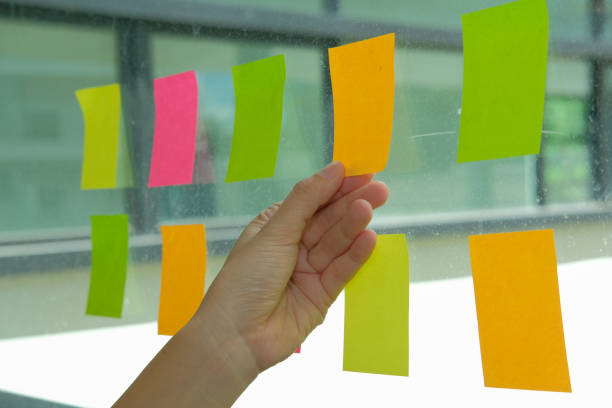 istock hand hold adhesive notes on glass wall. Sticky note paper reminder schedule for creative idea & business brainstorming 1056972058