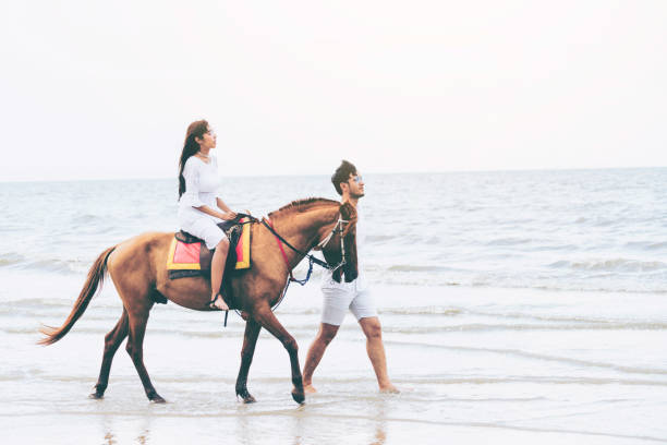 istock Young couple goes horse riding on tropical beach. 1056986482