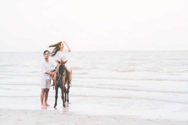 istock Young couple goes horse riding on tropical beach. 1056986790