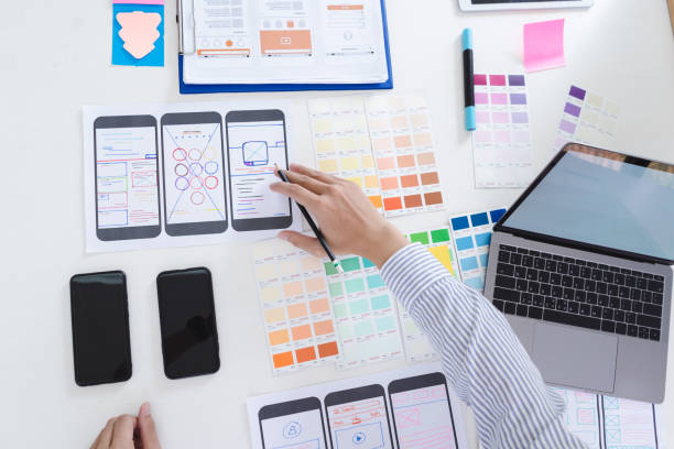 istock Creative ux designer designing screens for mobile responsive website development with UI/UX. Developing wireframe sketch layout design mockup on smartphone screen. 1056992126