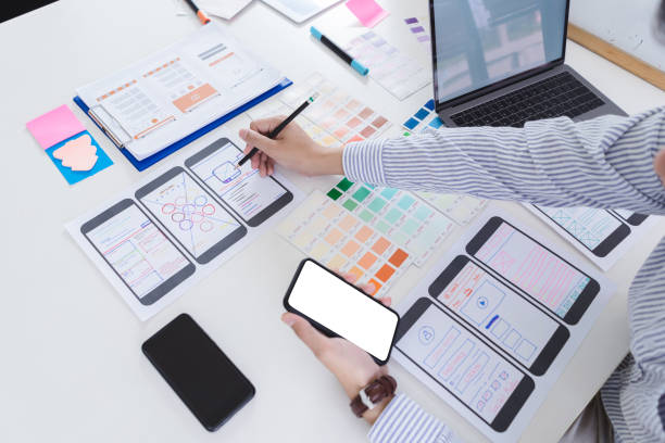 istock Creative designer hands sketching of screens for mobile responsive website development with UI/UX. Developing wireframe sketch layout design mockup on smartphone screen. 1056993168