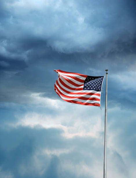 istock waving American flag at pole over cloudy storm sky 1057005654