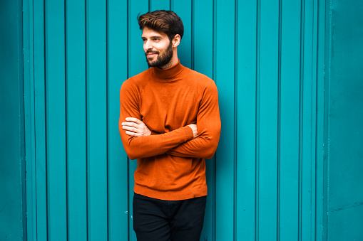 Portrait of smiling young man. He is wearing dark orange round neck sweater, on a green background