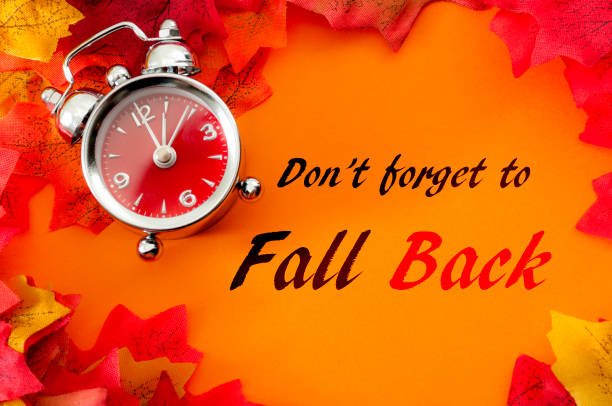Fall back, the end of daylight savings time and turn clocks back on hour concept with a clock surrounded by dried yellow leaves with the text Don't forget to fall back