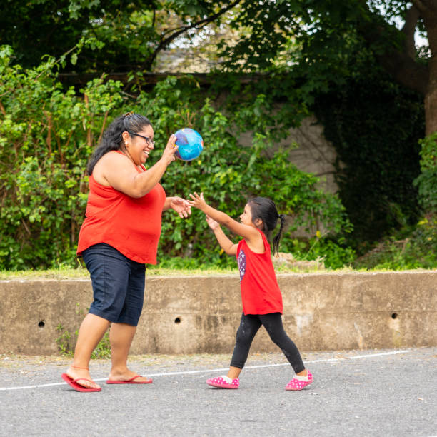 the body-positive, cheerful happy latino, mexican-american woman playing ball outdoor with her little daughter - family large american culture fun imagens e fotografias de stock