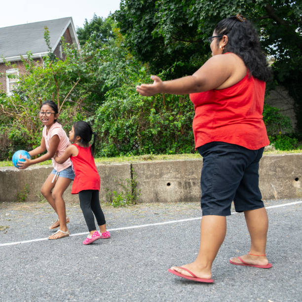 the big happy latino, mexican-american family - the mother, body-positive cheerful woman, and kids, girls of different ages - playing with a ball outdoor - family large american culture fun imagens e fotografias de stock
