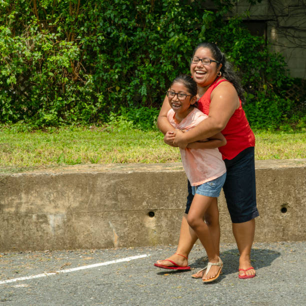 Latino, Mexican-American body-positive woman hugging her daughter outdoor Latino, Mexican-American body-positive woman hugging her daughter outdoor in the sunny hot summer day at the parking lot nearby his house in Pennsylvania, USA hot mexican girls stock pictures, royalty-free photos & images