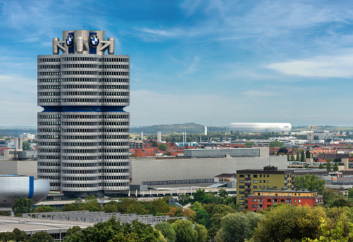 MUNICH, GERMANY - SEPT 7, 2018: The tower of the BMW (BMW-Vierzylinder or BMW-Turm) landmark serving as world headquarters for the Bavarian automaker. Architect, Karl Schwanzer. The Tower is 101m high and was built between 1968 and 1972. The tower has the shape of four cylinders in a car engine. In the Background the Allianz Arena (Fussball Arena Munchen, Schlauchboot), the home football stadium for FC Bayern Munich. Widely known for its exterior of inflated ETFE plastic panels, it is the first stadium in the world with a full colour changing exterior.