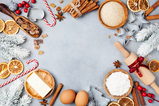 Bakery background with ingredients for cooking christmas baking decorated with fir tree. Flour, brown sugar, eggs and spices top view. Copy space for recipe.