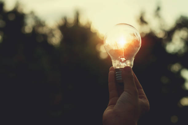 istock concept solar energy. hand holding lightbulb and sunset in nature 1057074102