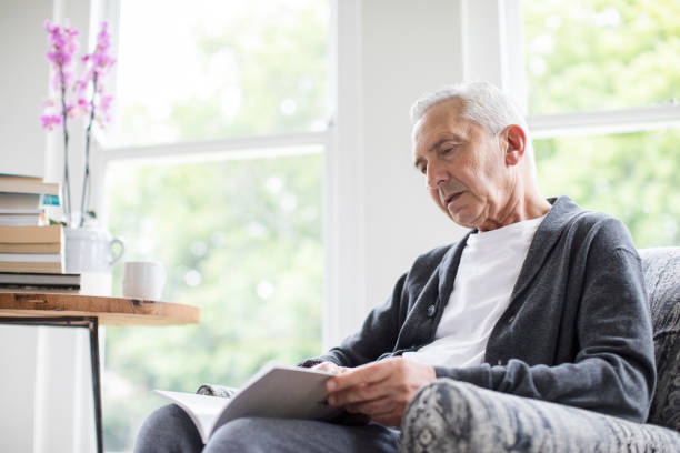 istock Senior man reading book while sitting on armchair 1057076058