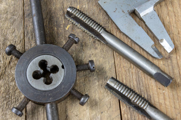 istock Metalwork tools on the workshop table. Threading dies and taps in an old dusty workshop. Black background. 1057078240