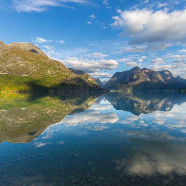 istock mountains mirrored in Geiranger fjord, blue sky, clouds 1057091080