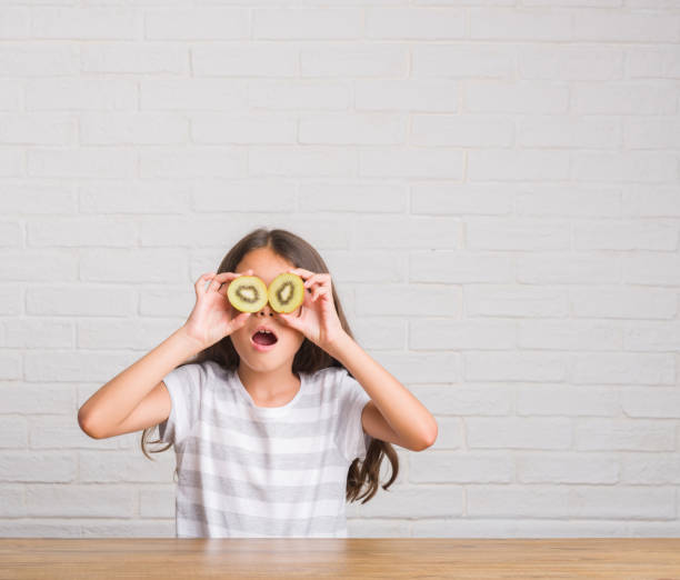 istock Young hispanic kid sitting on the table eating kiwi scared in shock with a surprise face, afraid and excited with fear expression 1057103108