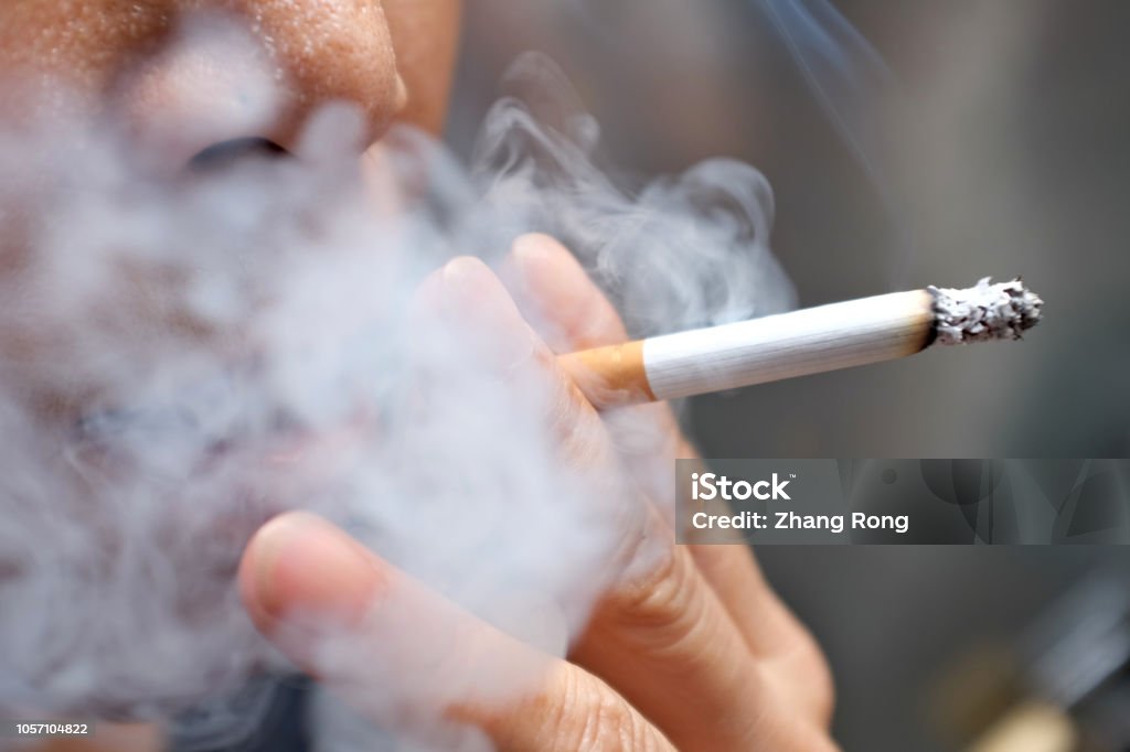 Smoking a cigarette Smoking a cigarette with smoke around and a blurred background Smoking Issues Stock Photo