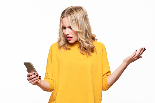 Shocked angry young woman looking at her mobile phone in disbelief. Woman staring at shocking text message on her phone, isolated over white background.