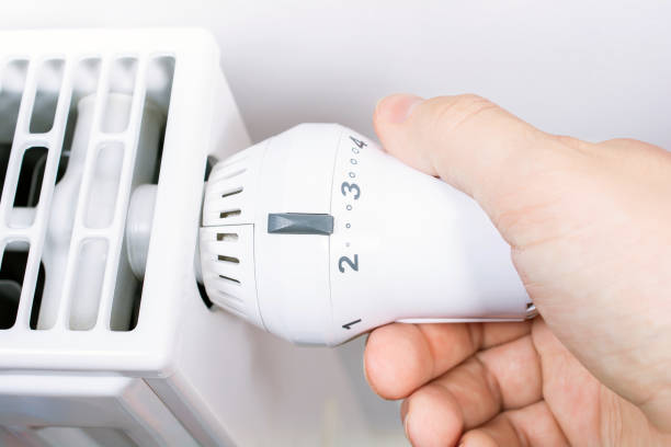 A Male Hand Turns The Radiator Of A White Heater In The Living Room, Saving Energy Concept stock photo