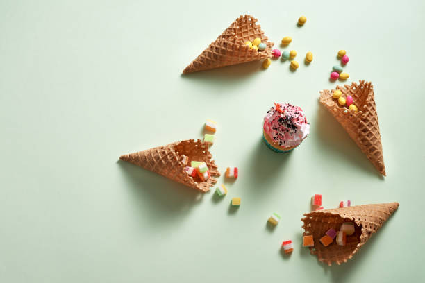 istock Round frame of assorted candy and waffle cones with cupcake on green background. Dessert concept. Flat lay, top view 1057114334