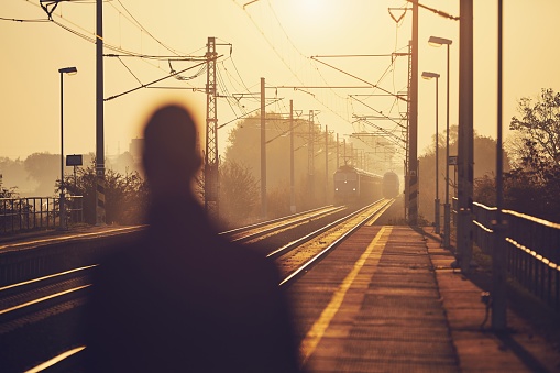 Silhouette of man waiting at railroad station platform at sunrise.